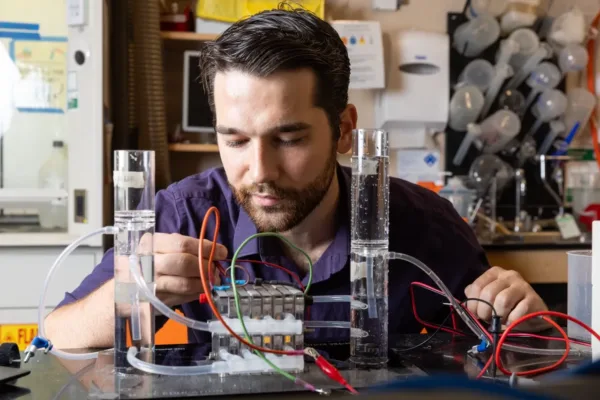 Man sitting at lab bench with mechanical device of two tubes filled with water